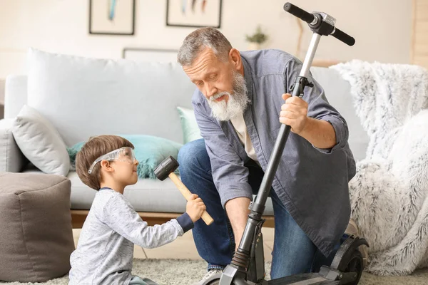 Cute little boy with grandfather repairing kick scooter at home — Stock Photo, Image