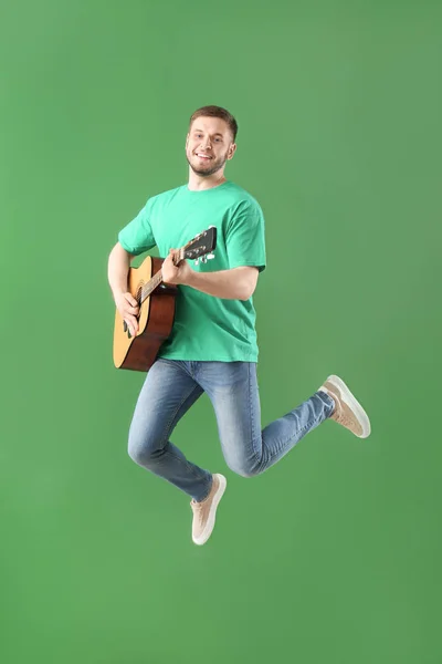 Guapo saltando joven con guitarra contra la pared de color —  Fotos de Stock