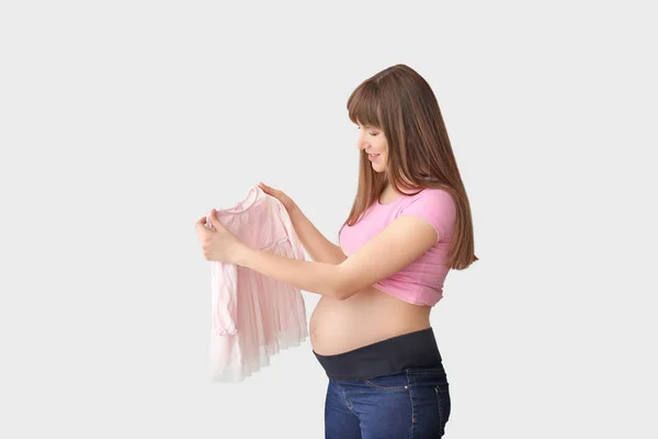 Junge schwangere Frau mit Babykleid auf hellem Hintergrund — Stockfoto