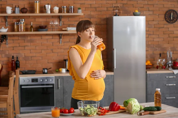 Молода вагітна жінка п'є сік на кухні — стокове фото