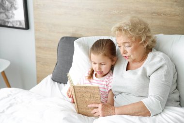 Sevimli küçük kız evde yatakta büyükanne ile kitap okuma