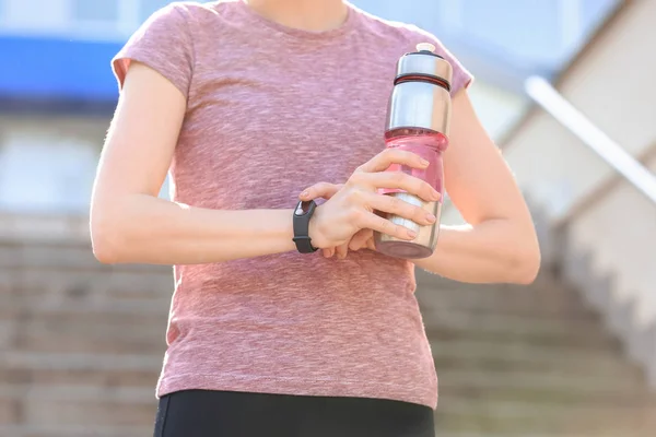 Sporty young woman with bottle of water checking pulse outdoors — Stock Photo, Image