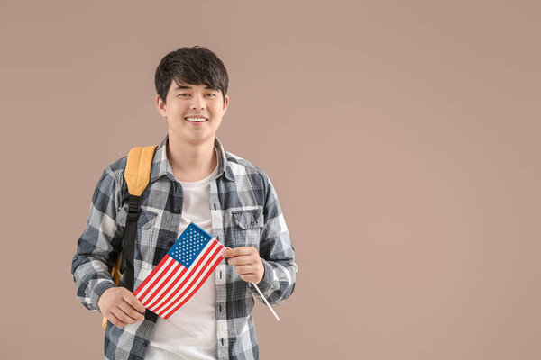 Young Asian student with USA flag on color background