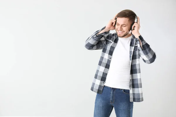 Handsome young man listening to music on light background — Stock Photo, Image