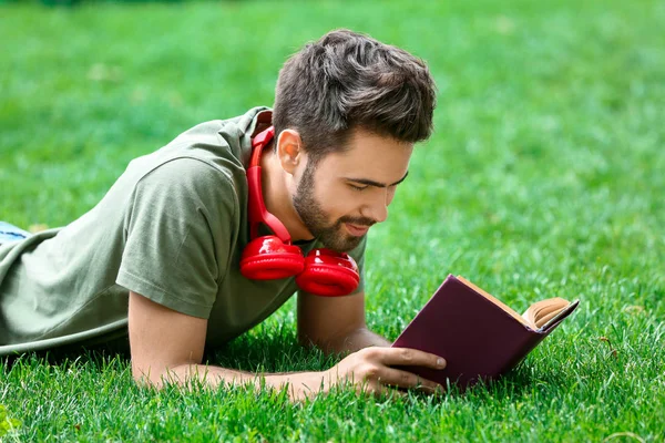 Jonge man luisteren naar muziek en lezen boek in Park — Stockfoto
