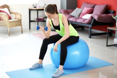 Genç kadın evde fitball ve dumbbell ile egzersiz yapıyor