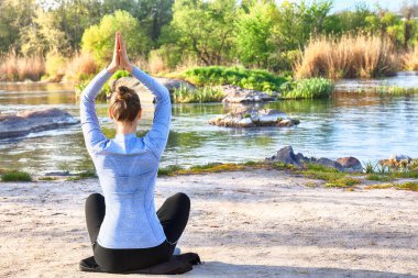 Güzel genç kadın nehir kenarında yoga yapıyor.