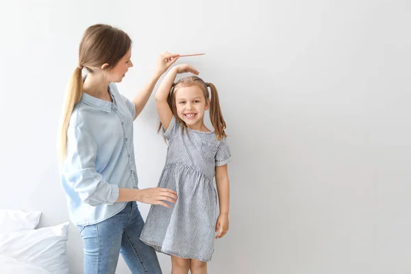 Ung mamma mäter höjden på sin lilla dotter nära ljus Wall — Stockfoto