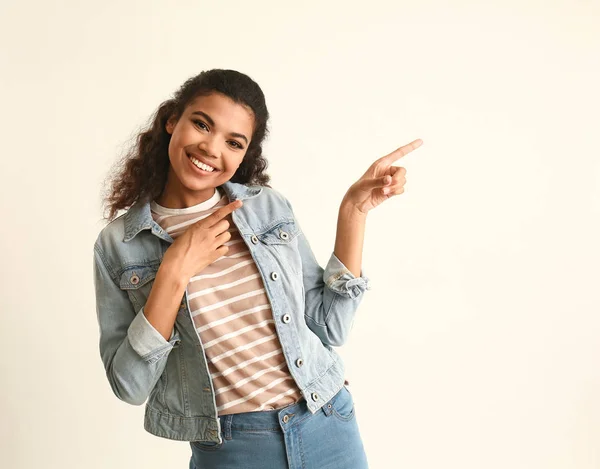 Ritratto di donna afro-americana carina che indica qualcosa su sfondo chiaro — Foto Stock