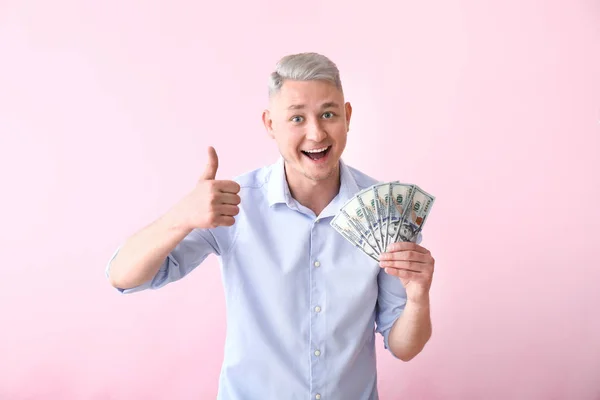 Happy young man with dollar banknotes showing thumb-up gesture on color background — Stock Photo, Image