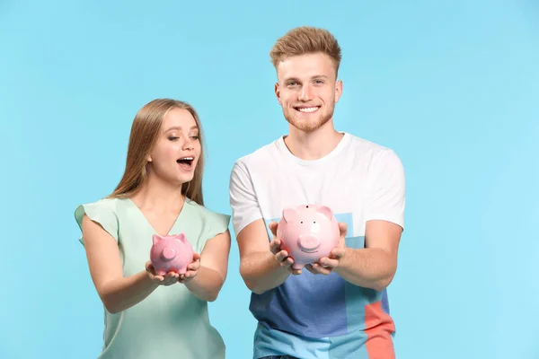 Happy couple with piggy banks on color background — Stock Photo, Image