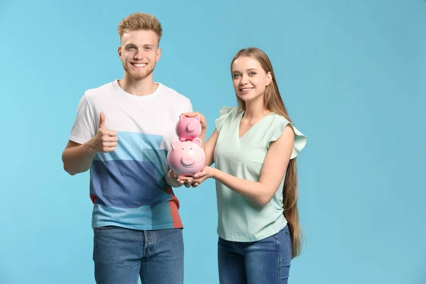 Happy couple with piggy banks on color background — Stock Photo, Image