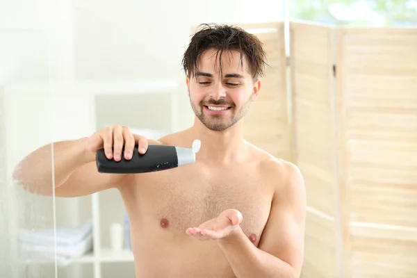 Hombre guapo con botella de champú tomando ducha en casa — Foto de Stock