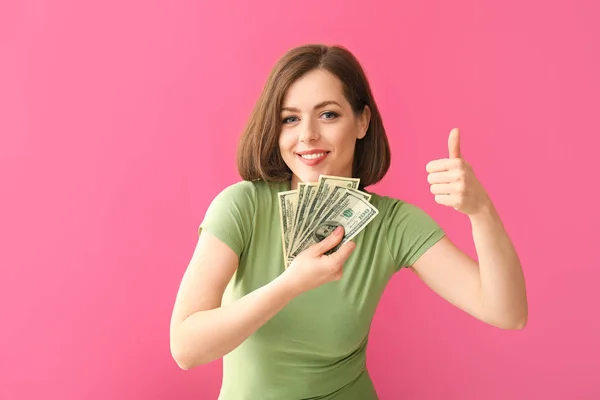 Beautiful young woman with money showing thumb-up on color background — Stock Photo, Image