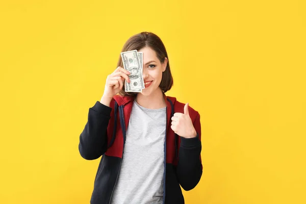 色の背景に親指を示すお金を持つ美しい若い女性 — ストック写真
