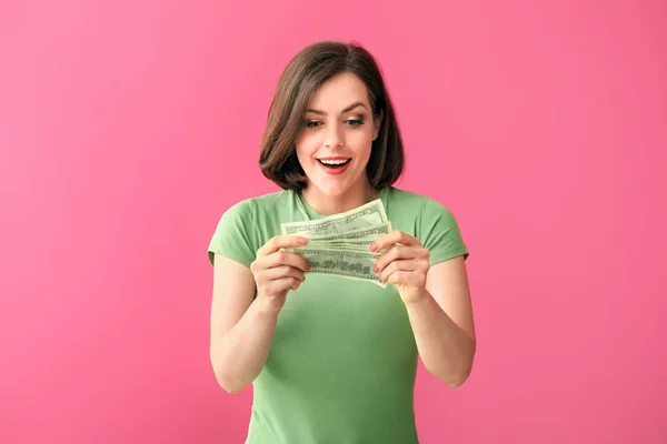 Excited young woman with money on color background — Stock Photo, Image