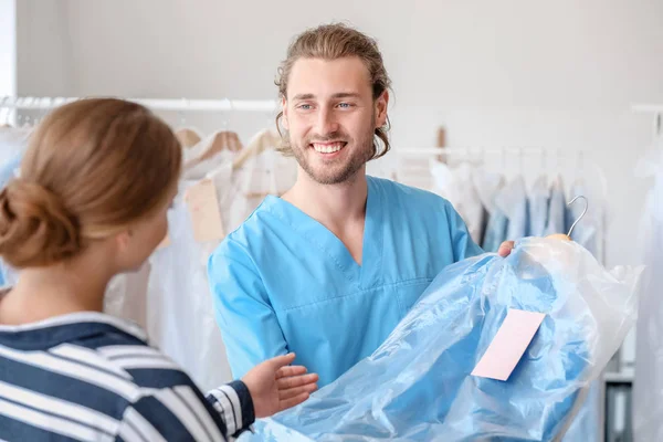 Hombre trabajador dando ropa al cliente en la moderna tintorería — Foto de Stock