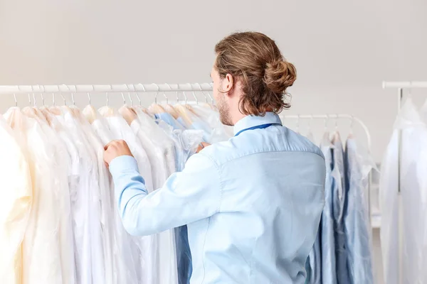 Worker of modern dry-cleaner's near rack with clothes — Stock Photo, Image