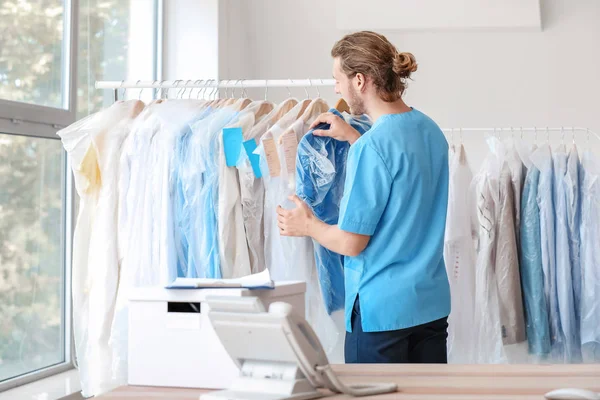 Worker of modern dry-cleaner's near rack with clothes