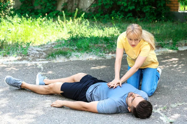 Woman giving CPR to unconscious man outdoors — Stock Photo, Image