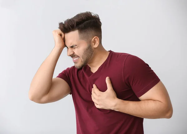 Young man suffering from heart attack on light background — Stock Photo, Image