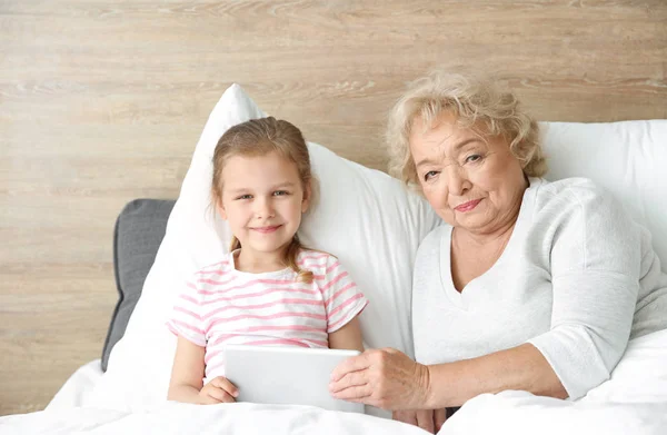 Linda niña con abuela usando tableta PC en la cama en casa —  Fotos de Stock