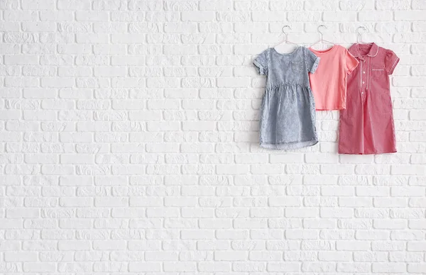 Hangers with clothes on white brick wall — Stock Photo, Image