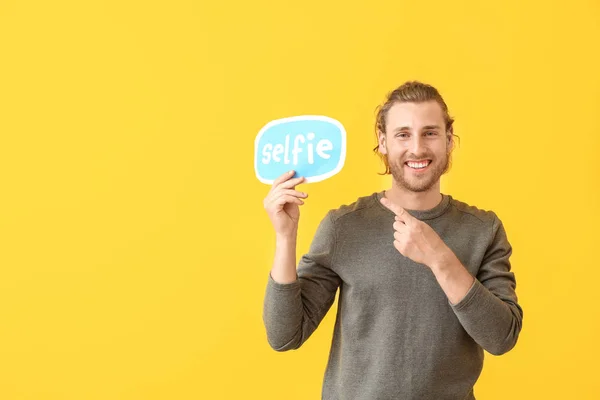 Male blogger holding paper with text SELFIE on color background — Stock Photo, Image