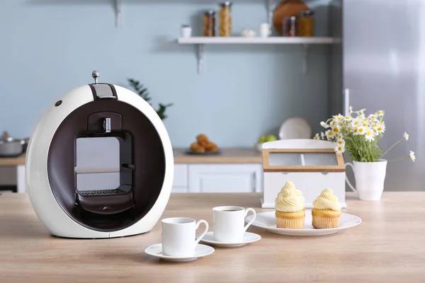 Moderne Kaffeemaschine mit Tassen und Cupcakes auf dem Tisch in der Küche — Stockfoto