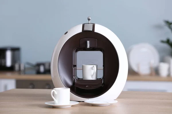 Современная кофеварка с чашками на столе на кухне — стоковое фото