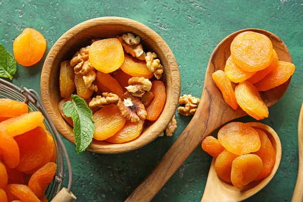 Bowl and spoons with dried apricots on color background — Stock Photo, Image