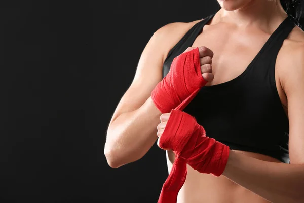 Sporty female boxer applying wrist bands against dark background