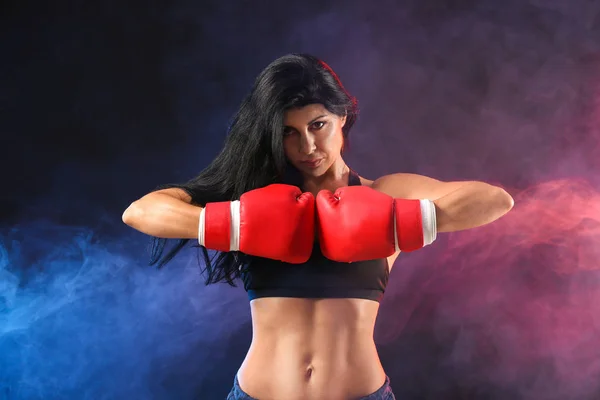 Sporty female boxer on dark background with color smoke