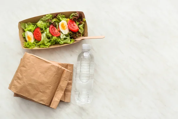 Fles water, papieren doos en tassen met heerlijk eten op lichte achtergrond — Stockfoto