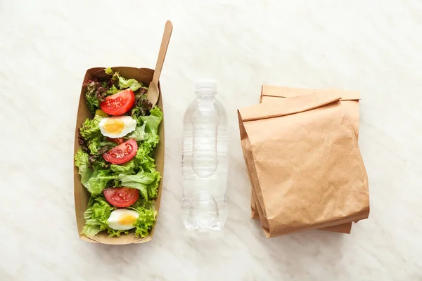 Fles water, papieren doos en tassen met heerlijk eten op lichte achtergrond — Stockfoto