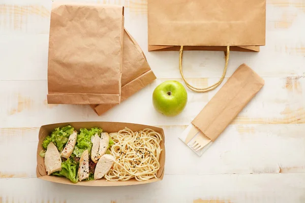 Papieren doos en tassen met heerlijk eten op witte houten achtergrond — Stockfoto