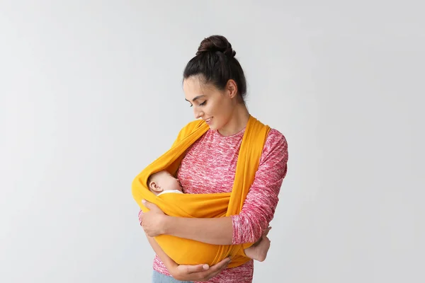 Young mother with little baby in sling on light background — Stock Photo, Image