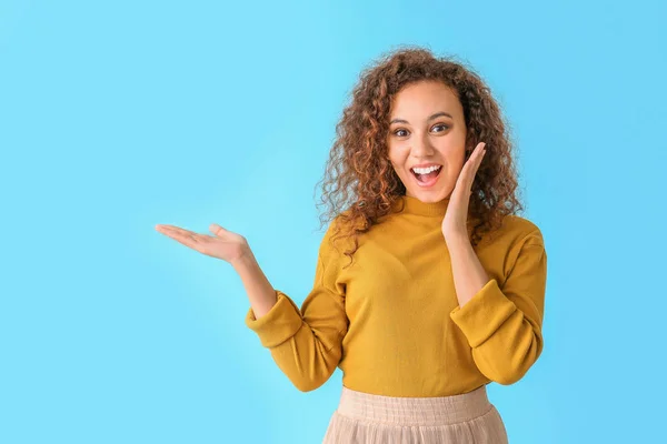 Surprised African-American woman showing something on color background — Stock Photo, Image