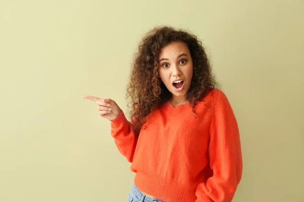 Shocked African-American woman pointing at something on color background — Stock Photo, Image