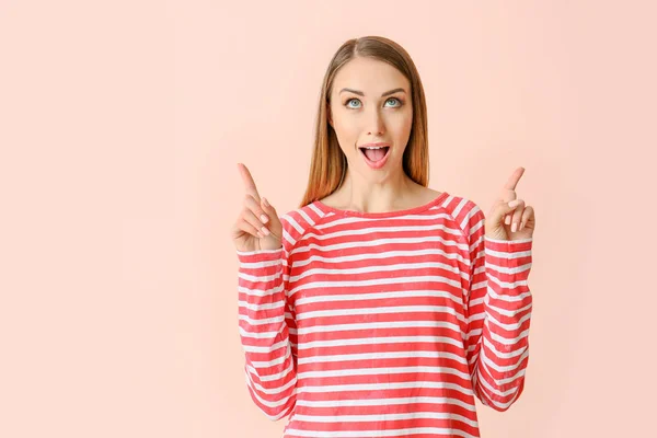 Beautiful young woman pointing at something on color background — Stock Photo, Image