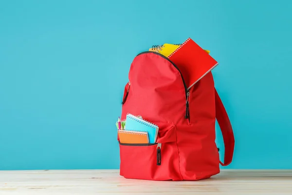 Zaino con materiale scolastico sul tavolo contro lo sfondo di colore — Foto Stock