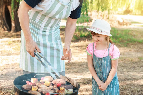 Little girl with father cooking tasty food on barbecue grill outdoors — Stock Photo, Image