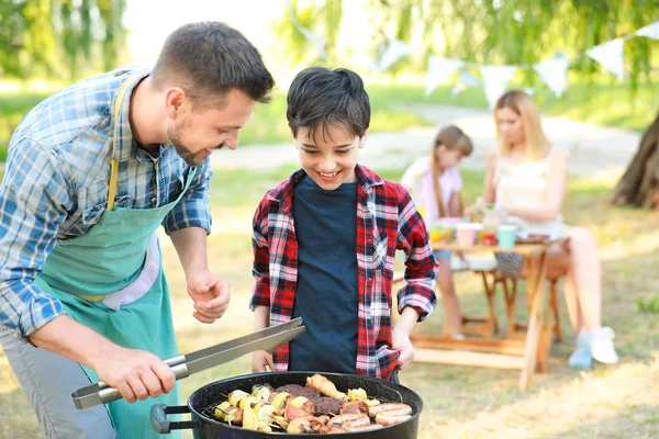 Kleiner Junge mit Vater kocht leckeres Essen auf Grill im Freien — Stockfoto