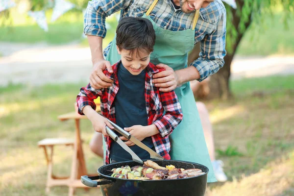 Little boy with father cooking tasty food on barbecue grill outdoors — Stock Photo, Image