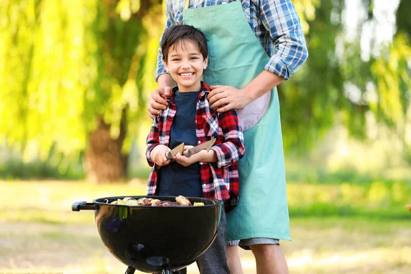 Menino com pai cozinhar comida saborosa em churrasqueira ao ar livre — Fotografia de Stock
