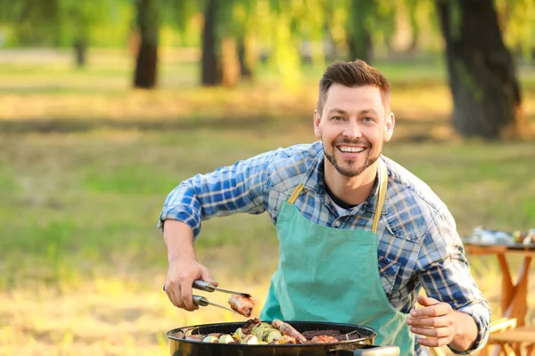 Homem cozinhar comida saborosa em churrasqueira ao ar livre — Fotografia de Stock