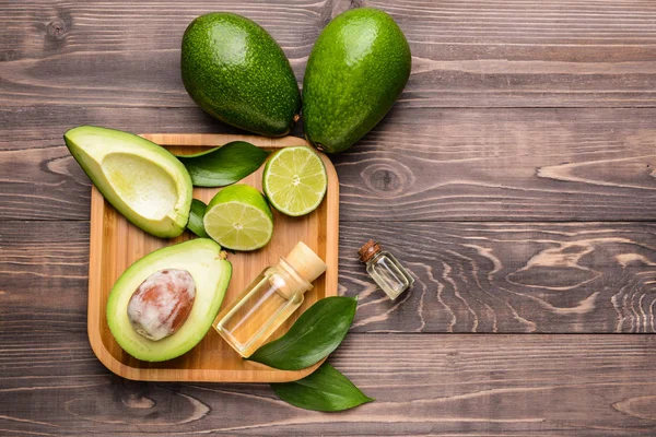 Plate with fresh ripe avocados, lime and essential oil on wooden table — Stock Photo, Image