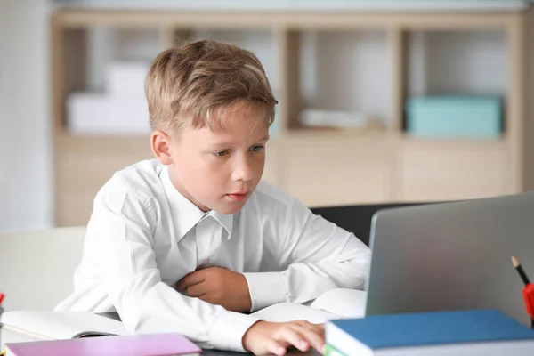 Симпатичный маленький школьник с ноутбуком делает уроки в классе — стоковое фото