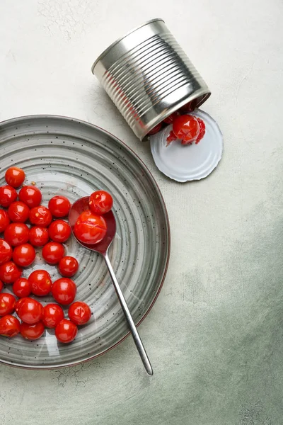 Tin can and plate with marinated tomatoes on grey background