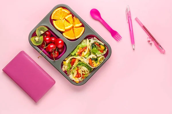 School lunch box with tasty food and stationery on color background